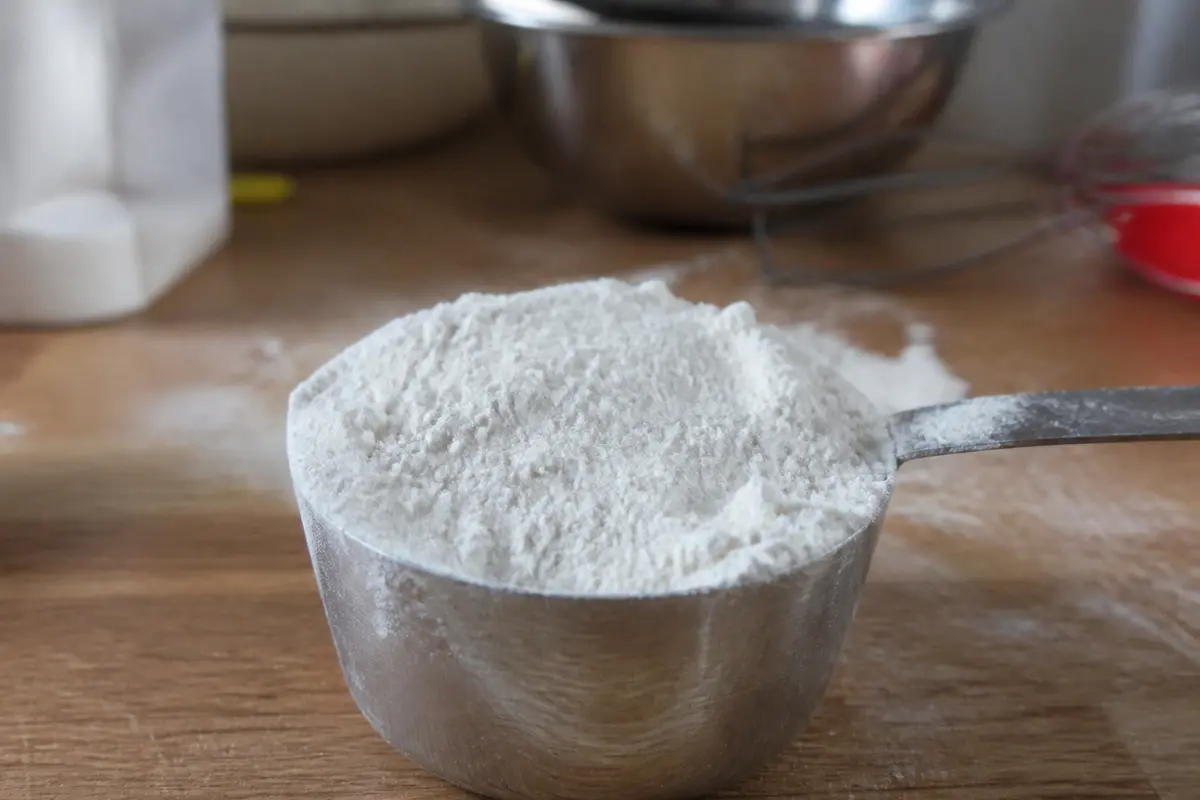 Mesure de farine de riz gluant dans une tasse en acier sur une table.