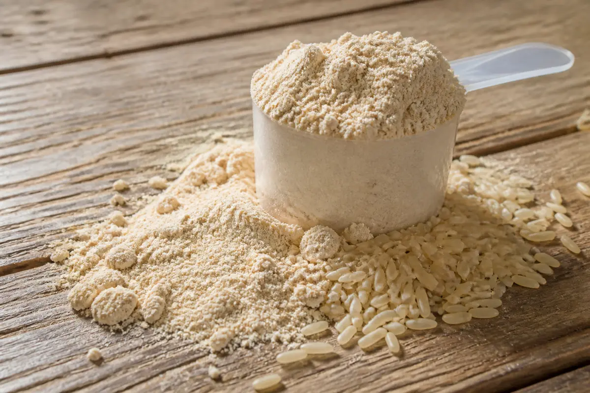 Mesurette de poudre et grains illustrant la protéine de riz sur une table en bois