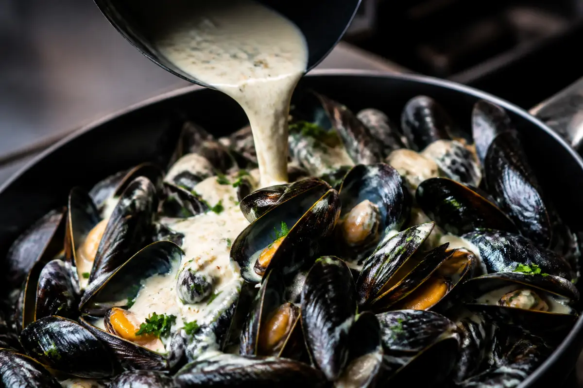Moules cuites avec une sauce au roquefort pour les moules versée fraîchement dessus
