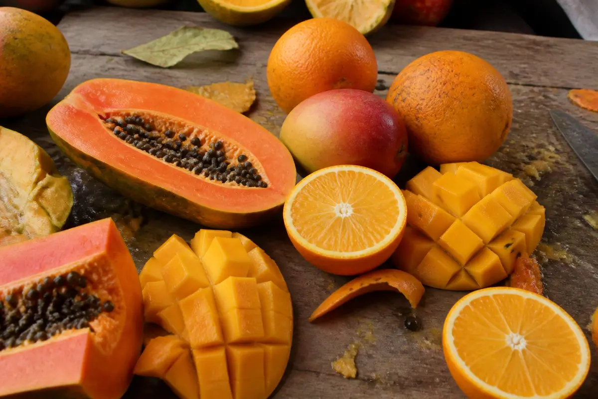 Assortiment de fruits exotiques orange : mangue, papaye, oranges tranchées et entières sur table boisée